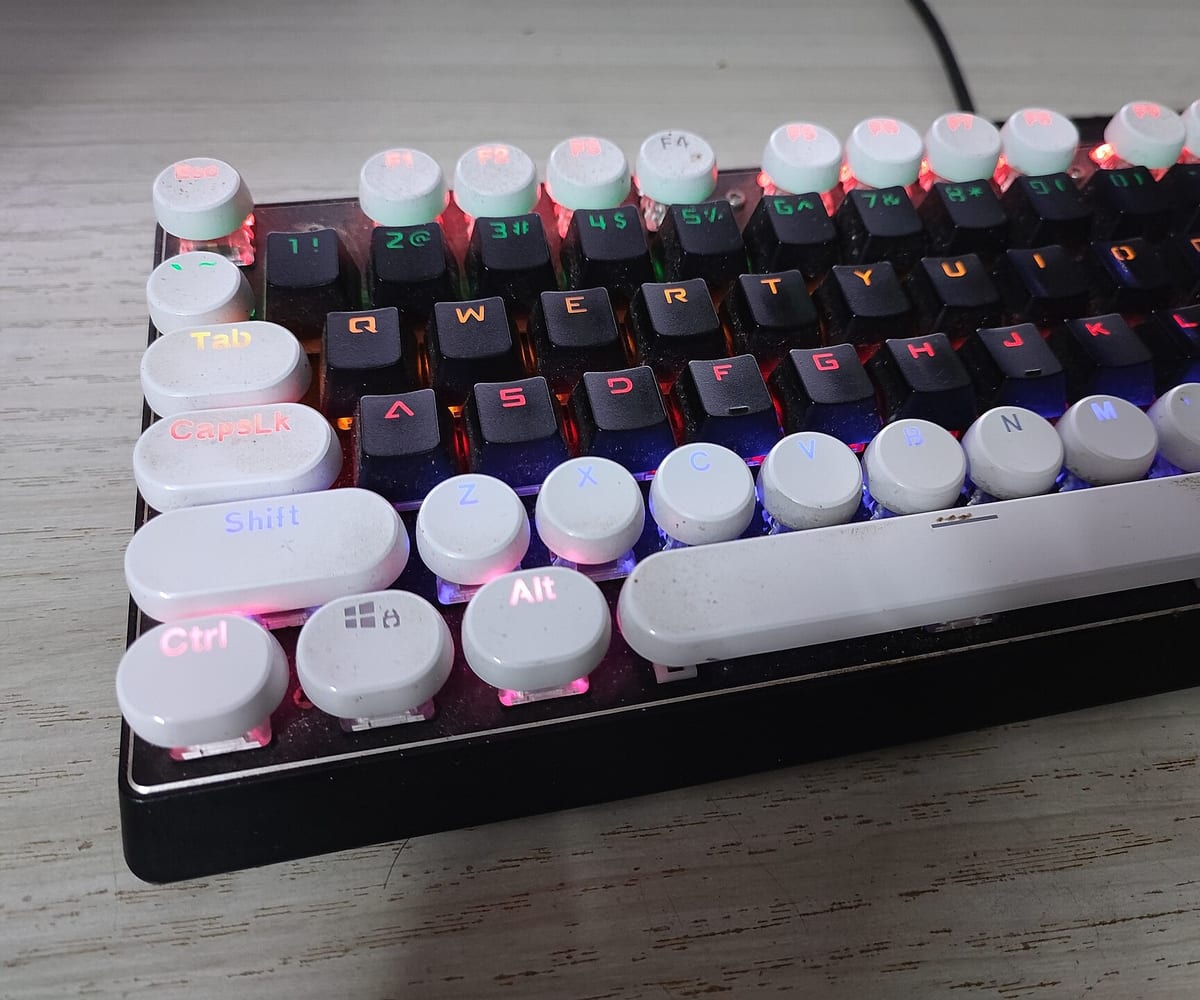 A mechanical keyboard with pale round keycaps and pink backlighting, seen at an angle.